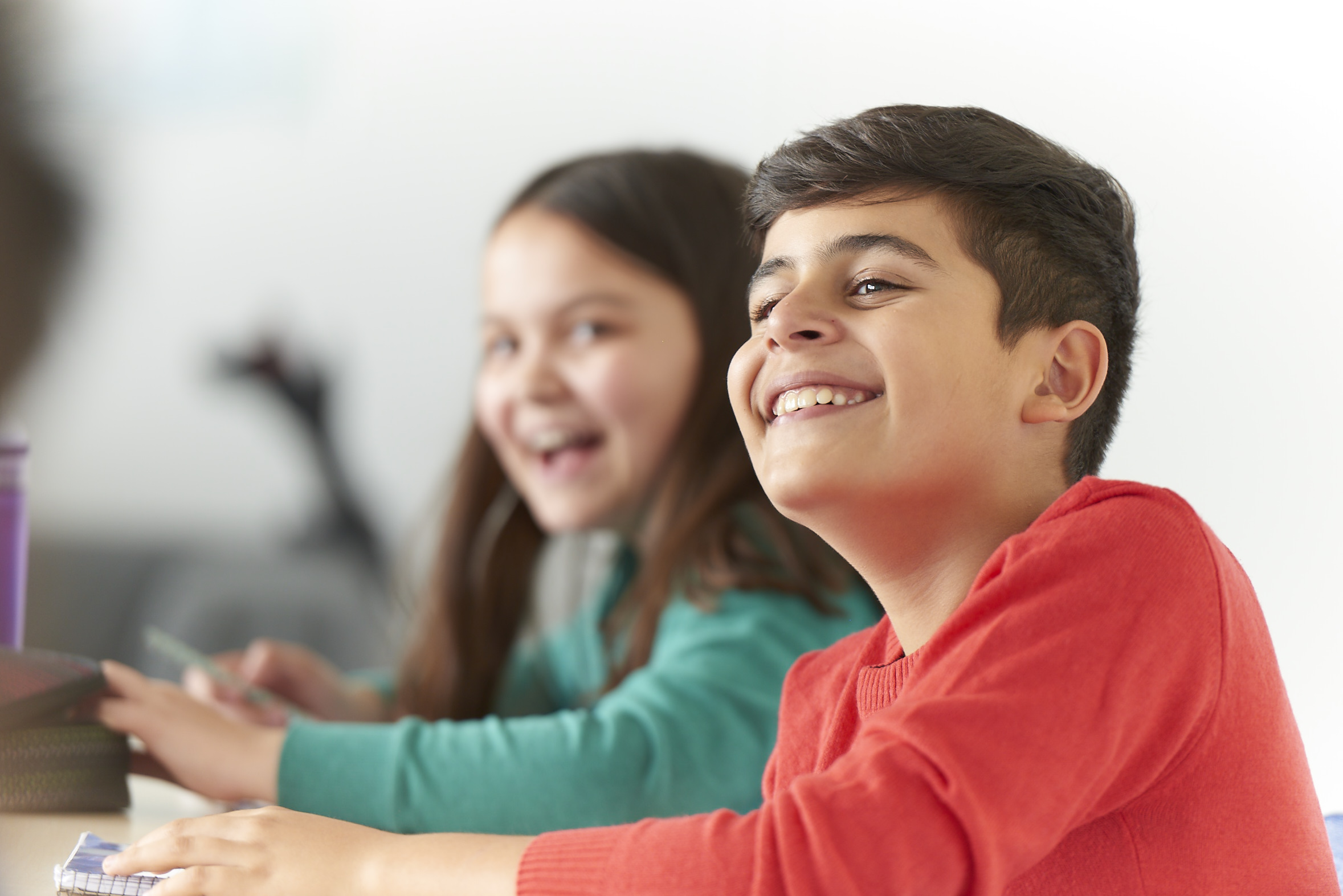 A girl in a green jumper and a boy in a red jumper laugh and look ahead.