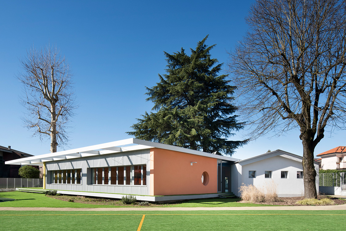 The school building from the outside. Grass can be seen in the front, three tall trees in the background.