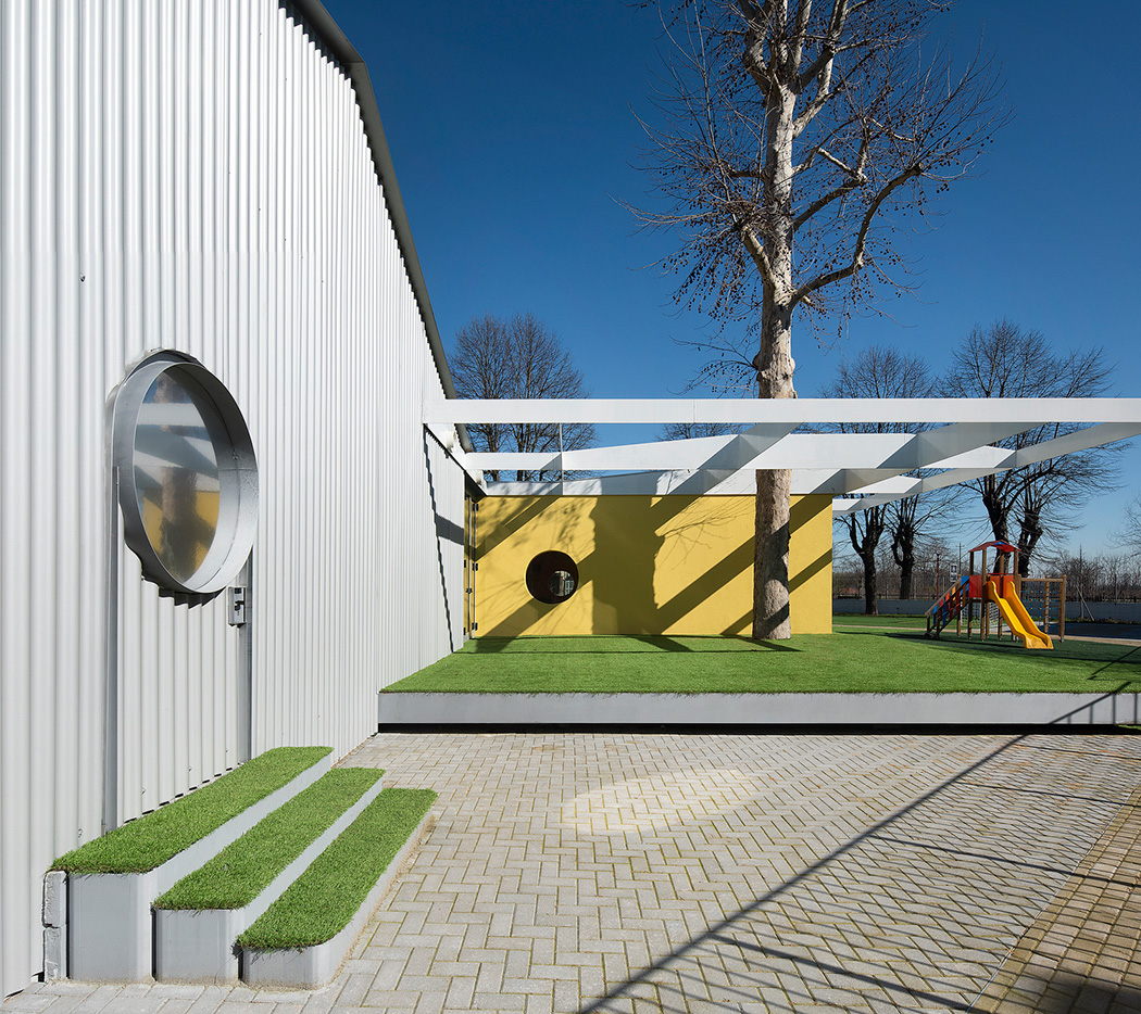 A play area in front of the school building with one part concrete and one part green space. 