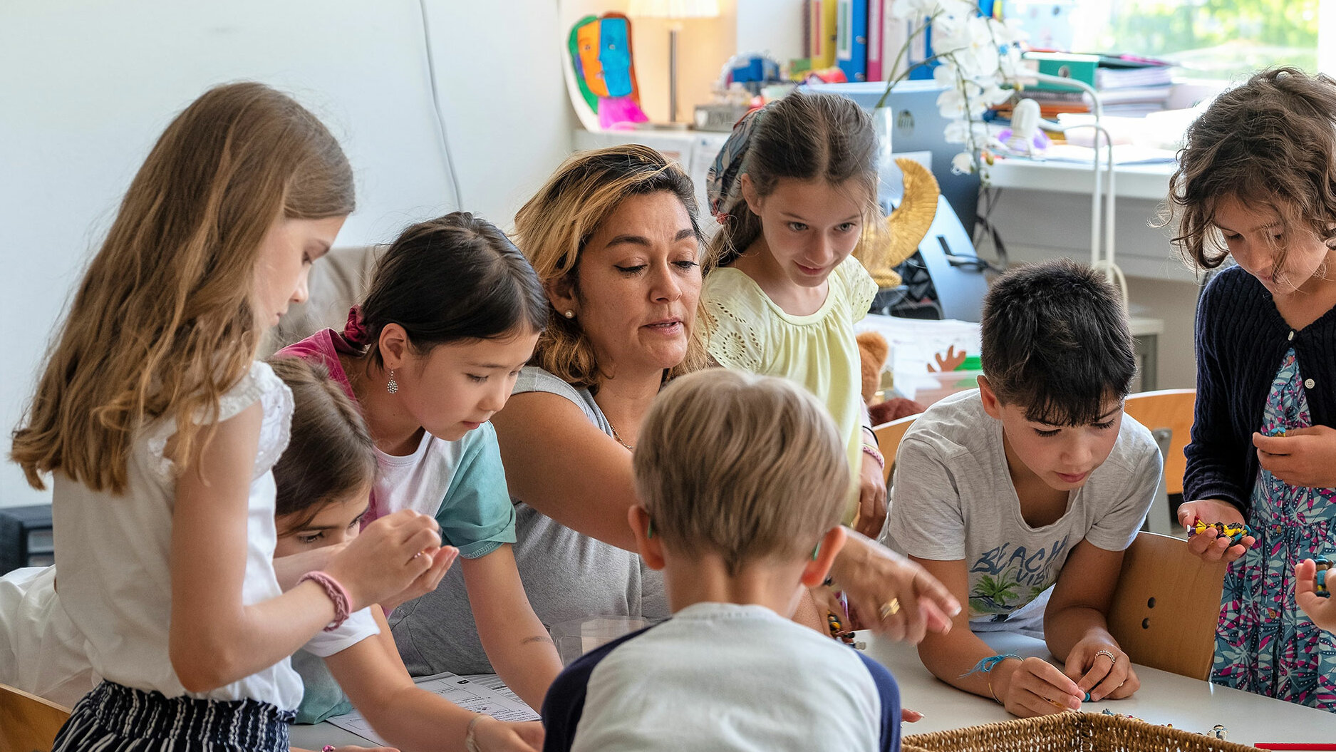 A teacher points at something and is surrounded by a group of primary school children.