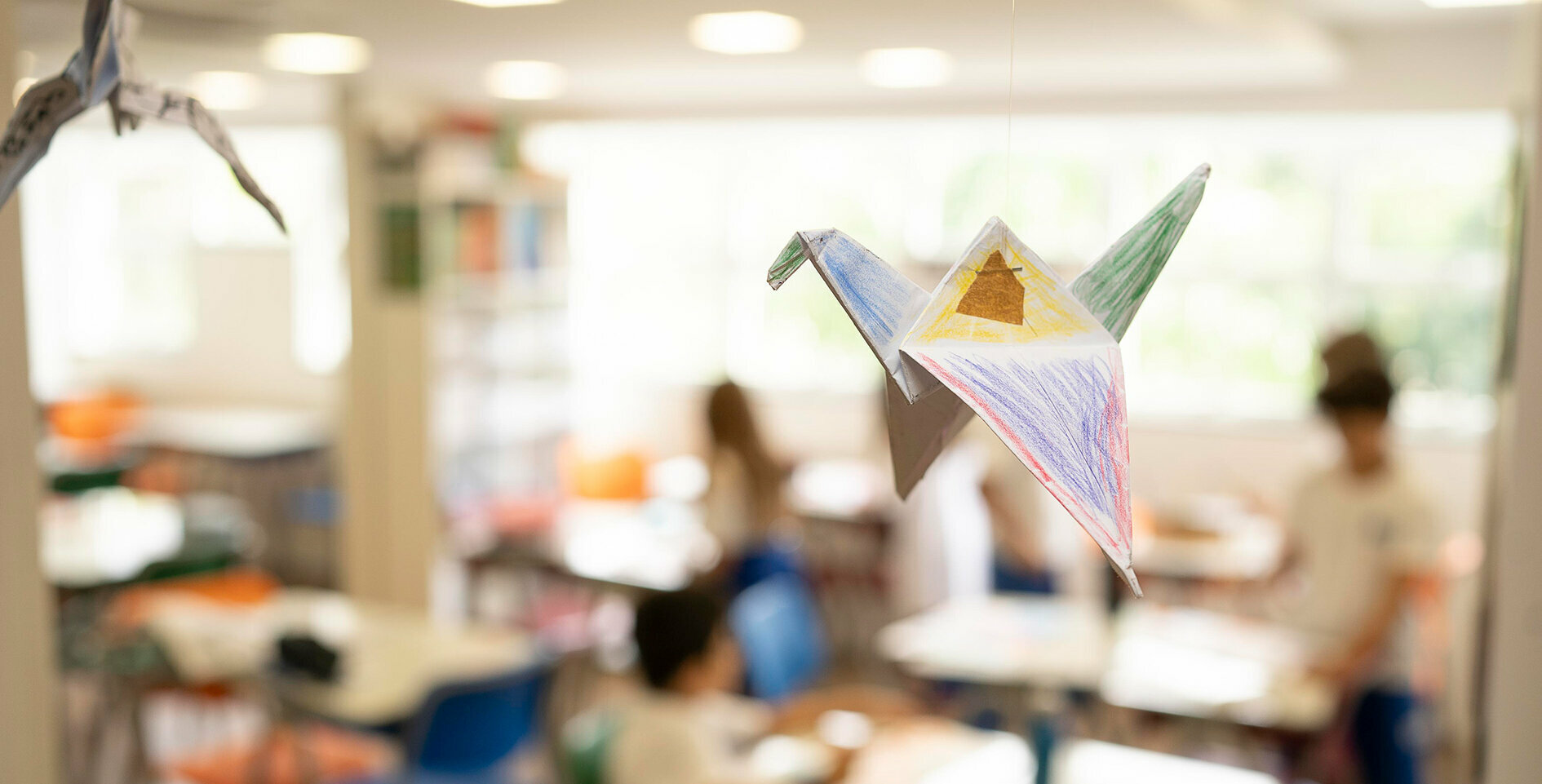 A handmade, painted origami crane hangs in the classroom, which fades into the background.