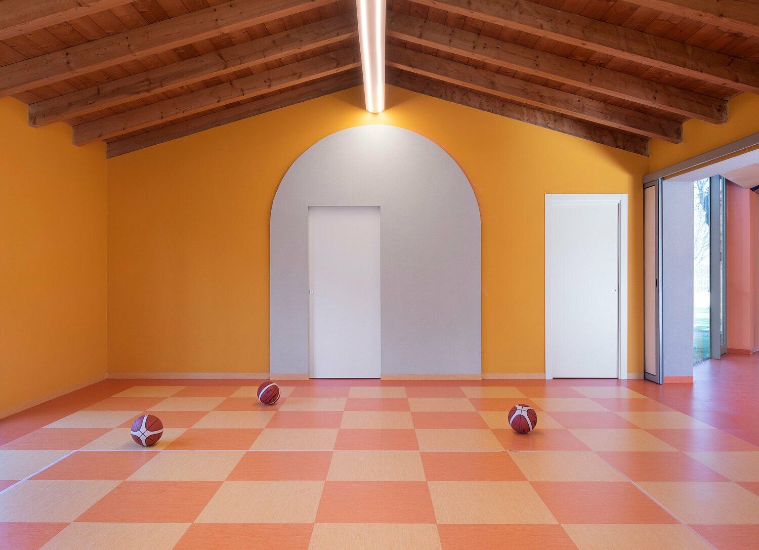 A large room for sports, designed in orange tones. There are three basketball balls on the floor.