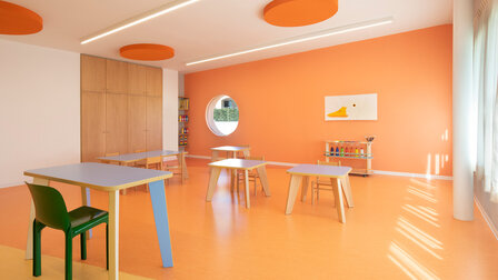 A modern, bright schoolroom with a round window and orange walls and floor.
